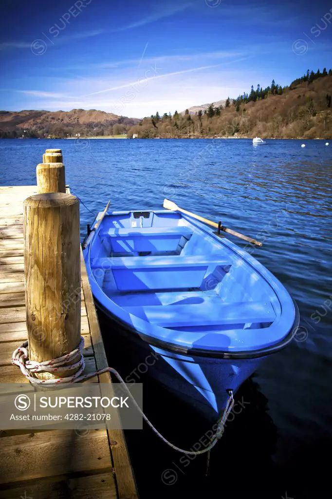 England, Cumbria, Windemere. A blue rowing boat moored to a jetty on Lake Windemere.