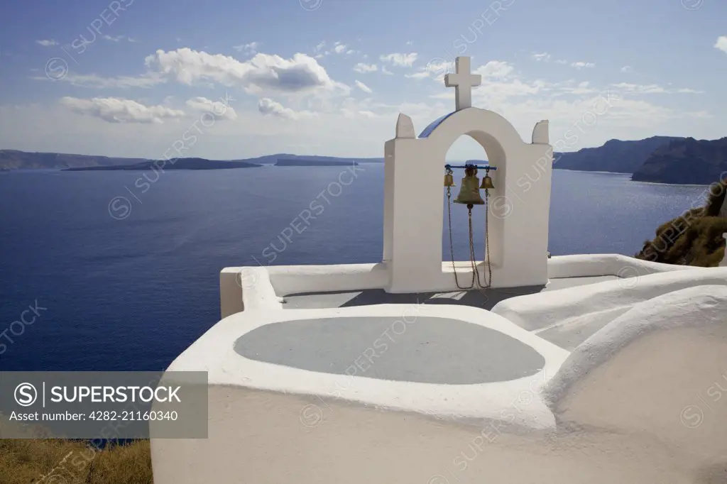 A view of a bell tower perched on a traditional roof overlooking the caldera.