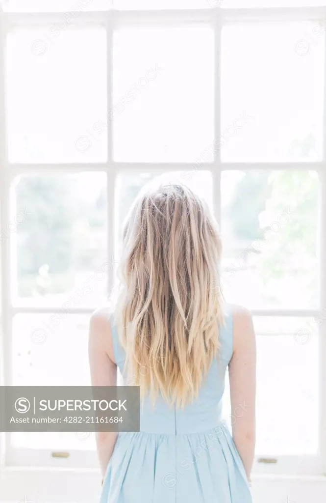 A blonde girl looking out of a window.