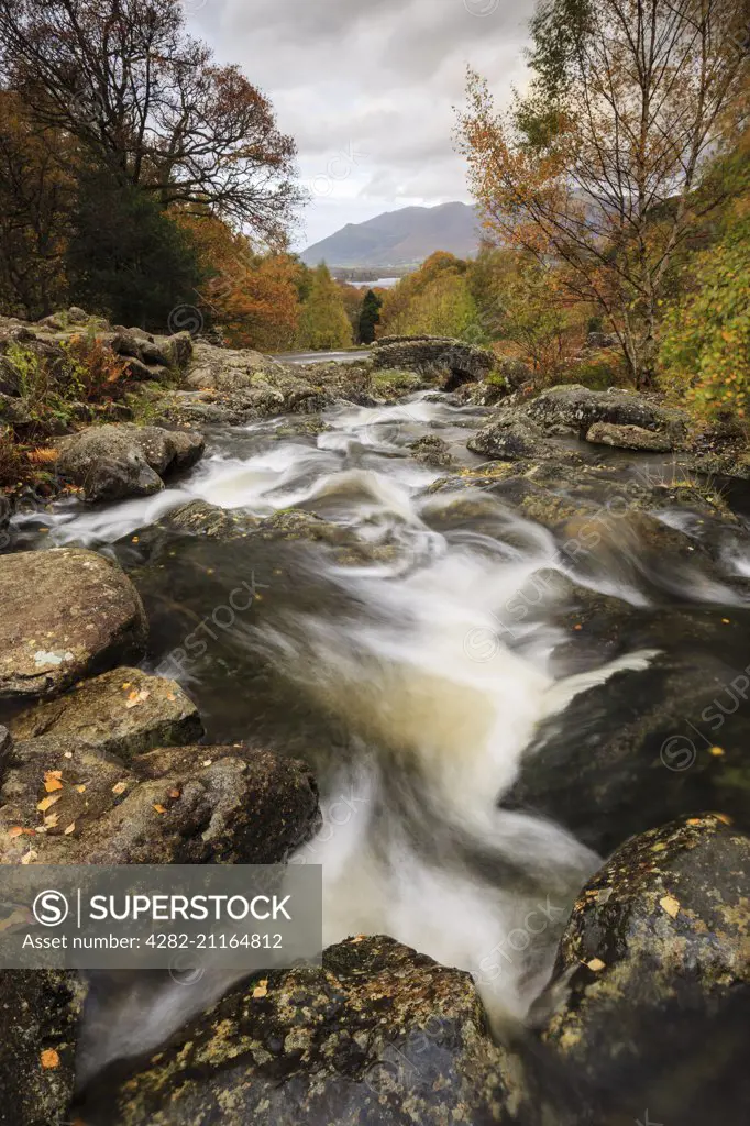 A river flowing towards an old stone bridge in the Lake District.