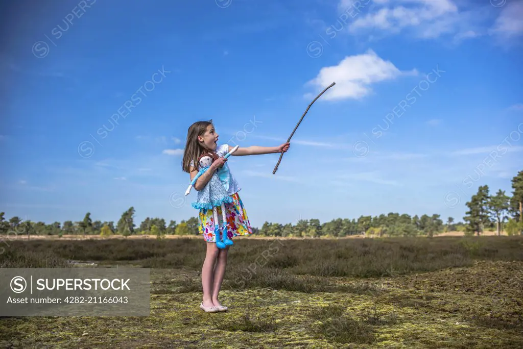 A young girl points at a cloud with a stick.