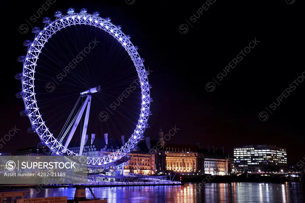 England, London, South Bank. A view across the River Thames to an illuminated London Eye at night.