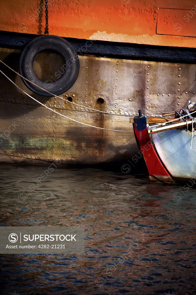 England, Cumbria, Maryport. The end of a small boat moored to the side of a large ship at Maryport Harbour.