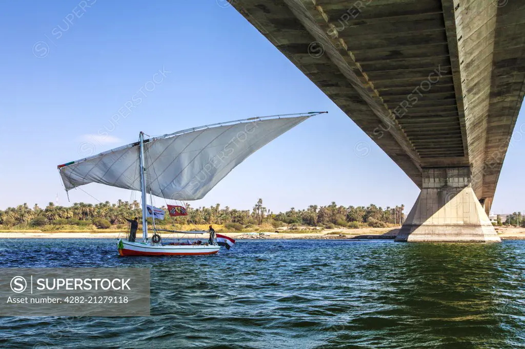Tourist felucca swivels its main sail as it passes under the bridge at Aswan on the Nile in Egypt.