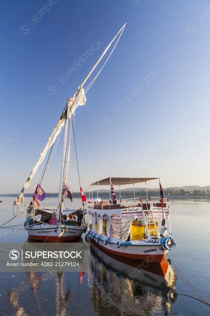Tourist felucca and support boat moored along the bank of the Nile near Aswan at sunrise.