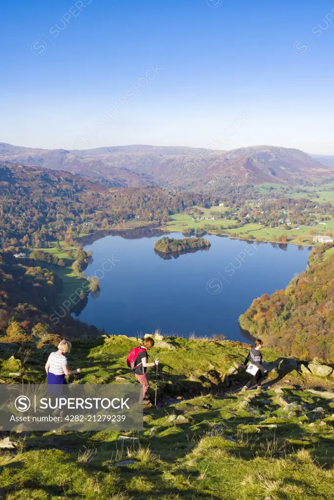 Walkers descending the north western slope of Loughrigg Fell in the Lake District with Grasmere lake beyond.