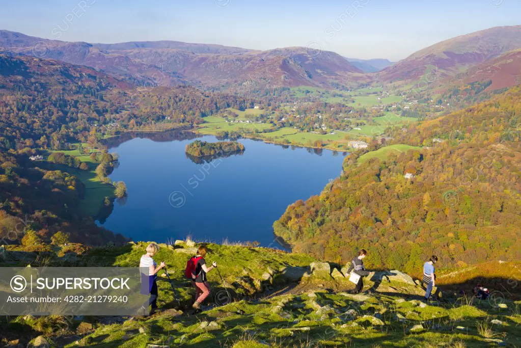 Walkers descending the north western slope of Loughrigg Fell in the Lake District with Grasmere lake beyond.