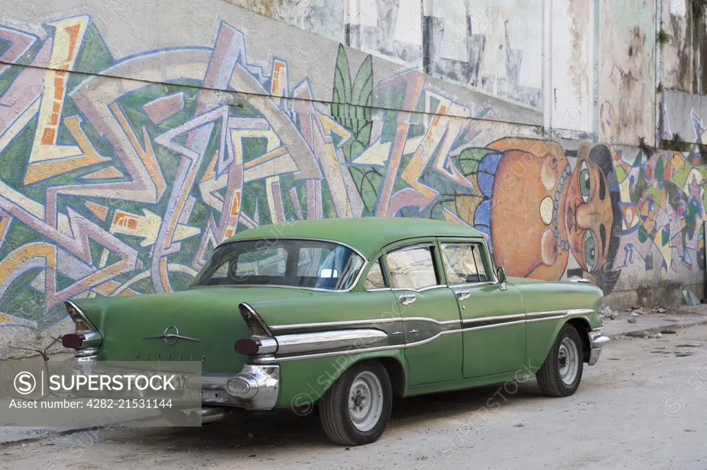 Green American Pontiac car set against wall of graffiti.