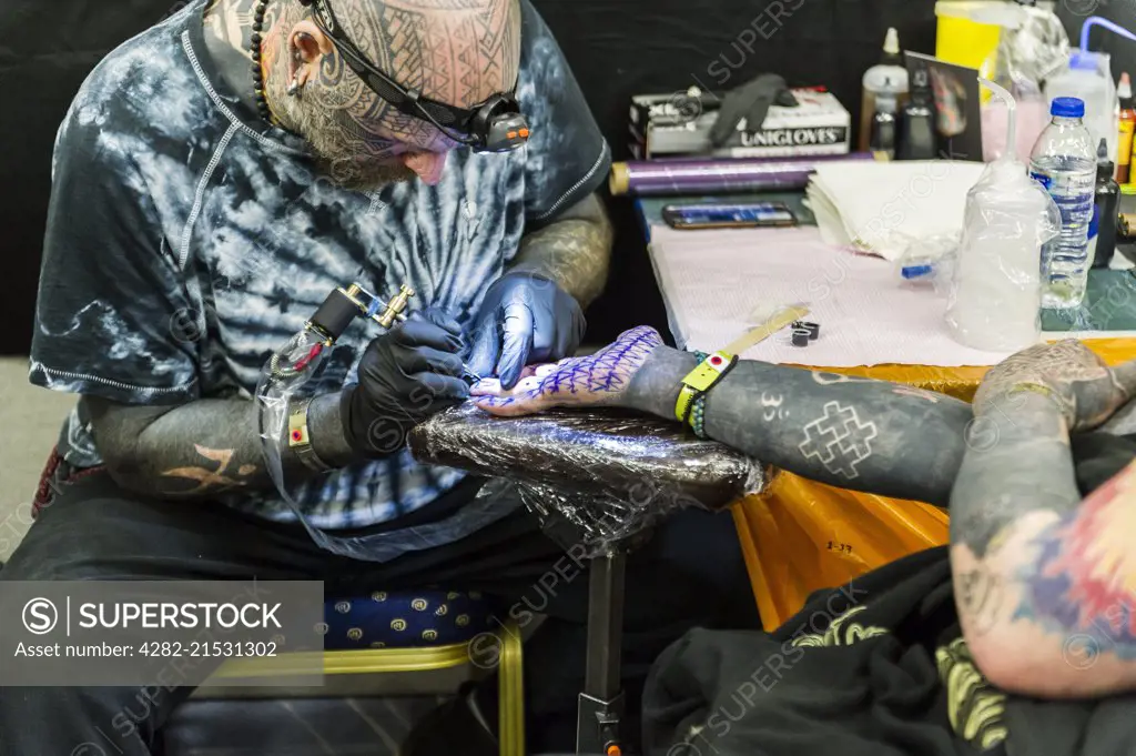 A man being tattooed on the palm of his hand.