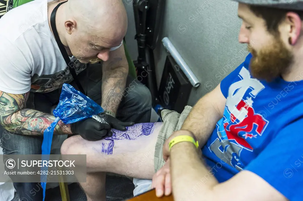 A man being tattooed on his leg.