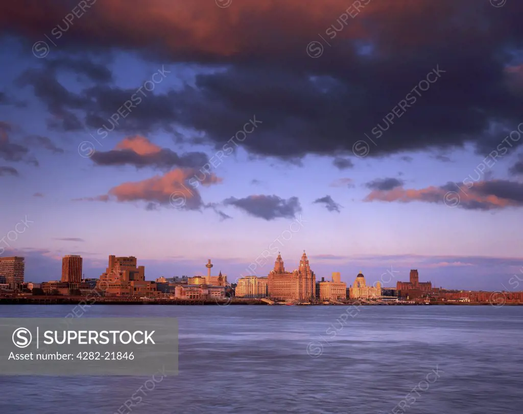 England, Merseyside, Liverpool. View across the River Mersey towards the Three Graces on the Liverpool waterfront at sunset.