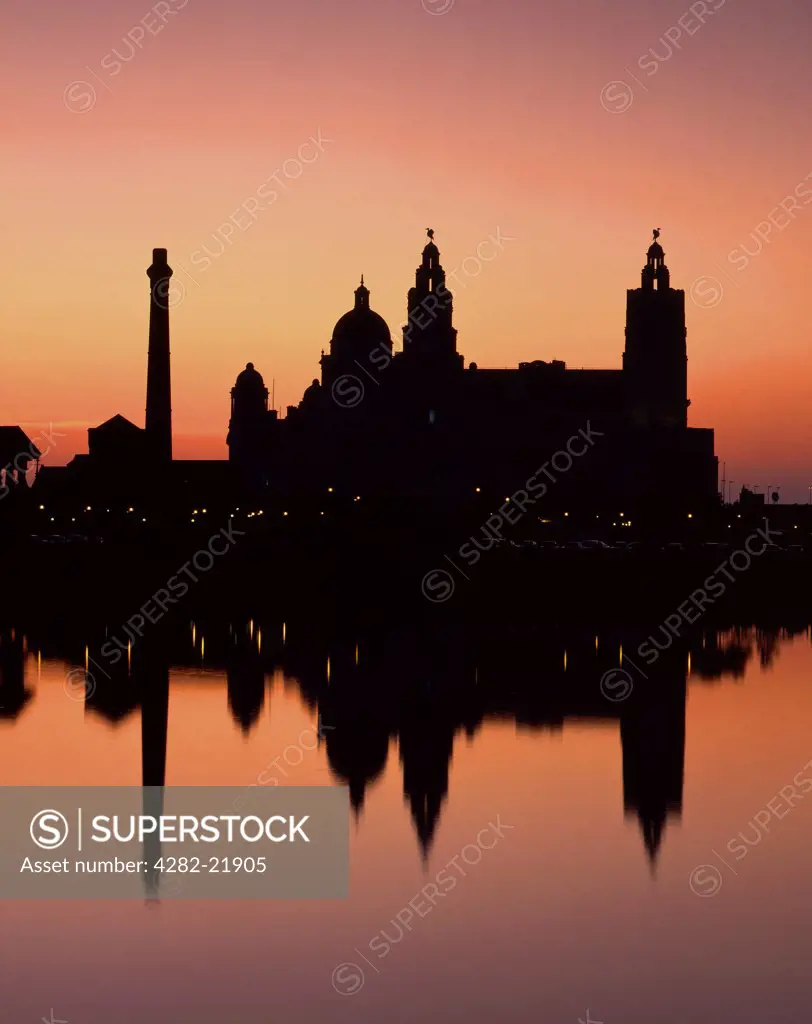 England, Merseyside, Liverpool. Silhouette of the Royal Liver Building, one of the most recognisable landmarks in the city of Liverpool, reflected in the River Mersey at sunset.