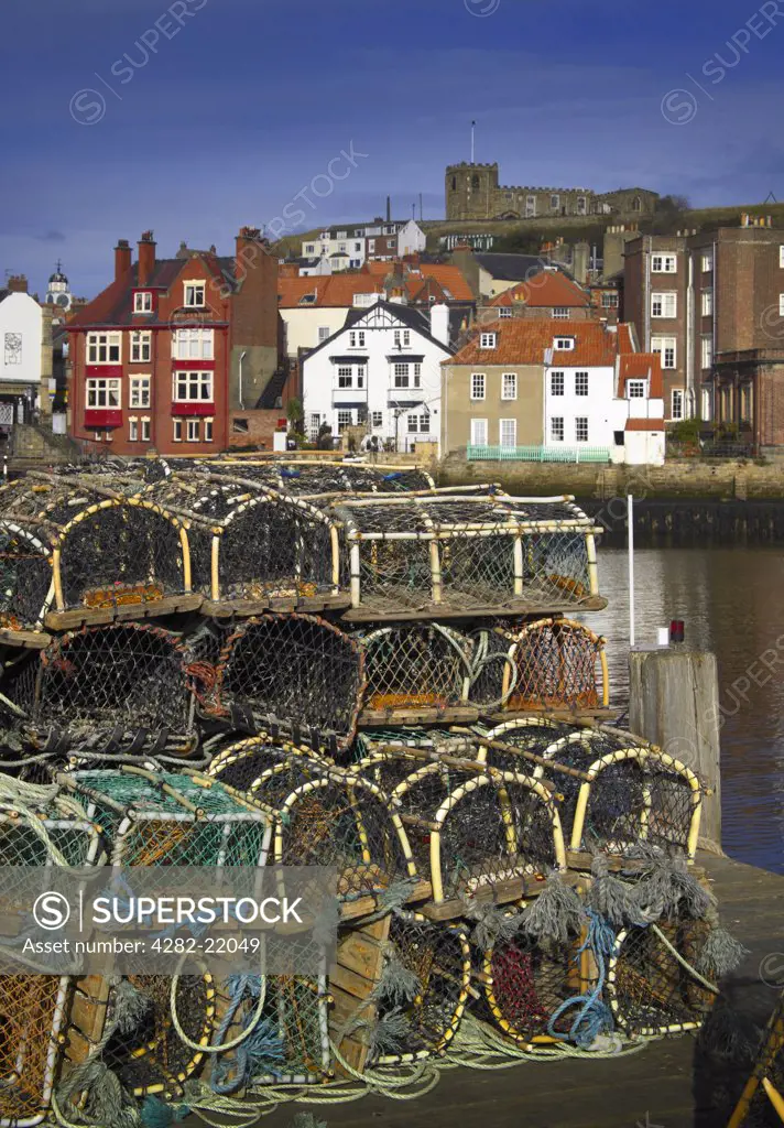England, North Yorkshire, Whitby. Lobster pots on the quayside with St Mary's Church and the town behind.