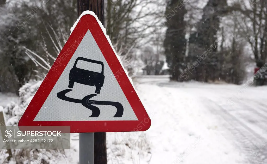 England, Essex, Saffron Walden. A rural slippery road sign with a snow covered road in the background in Essex.