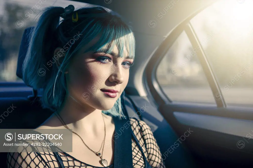 Portrait of teen girl with blue hair and pierced nose in the backseat of a car while on a roadtrip.