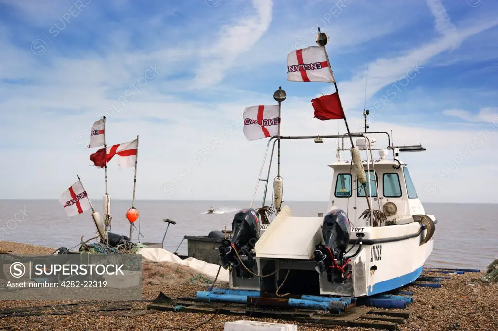 England, Suffolk, Aldeburgh. England flags flying from a fishing boat and equipment on the beach at Aldeburgh.