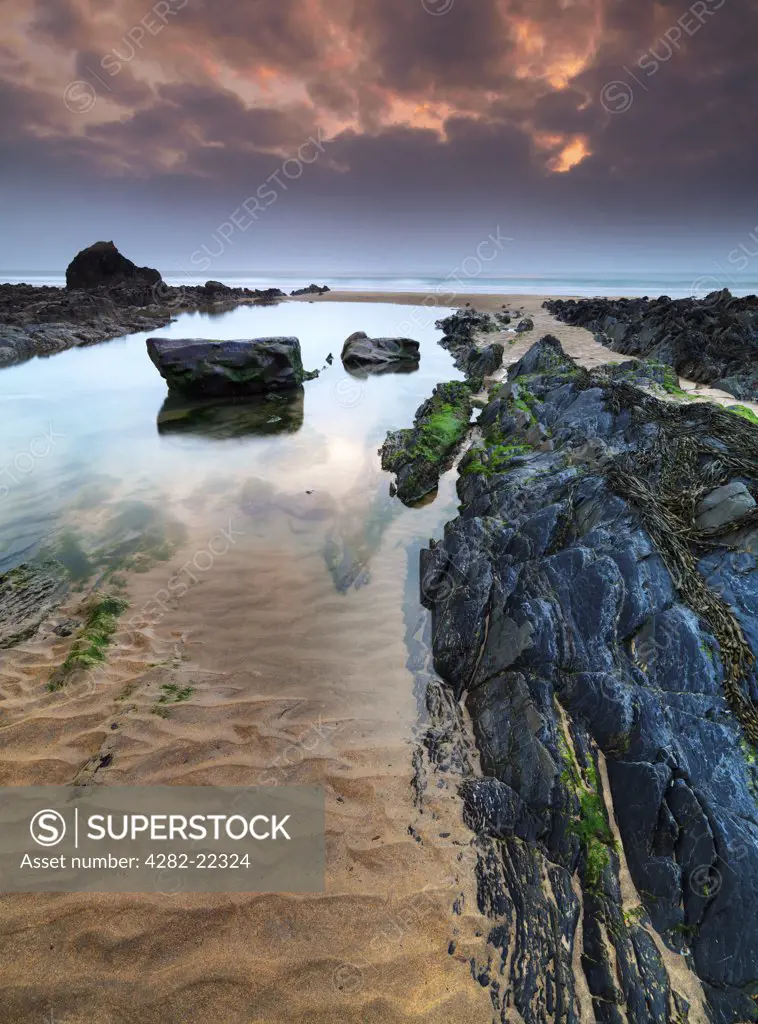 England, Cornwall, Sandy Mouth. Rock formations and pools of water on Sandy Mouth beach at dusk.