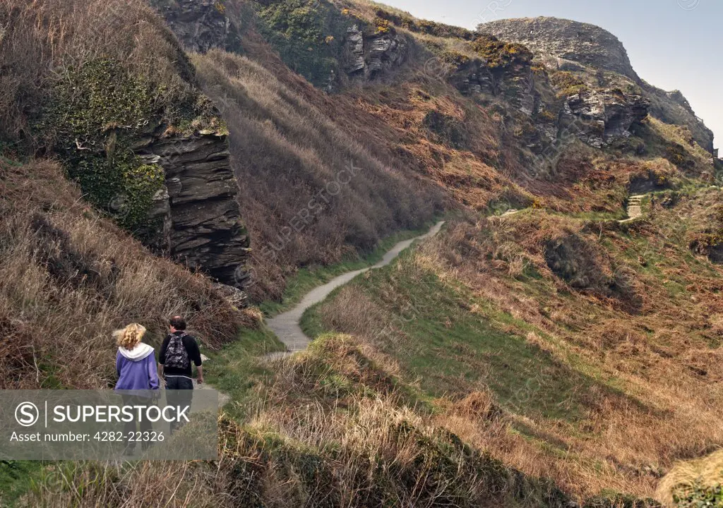England, Cornwall, Tintagel. A couple walking along a path leading to Tintagel Castle on the rugged North Cornwall coast. Tintagel Castle is steeped in legend and said to be the birthplace of King Arthur.