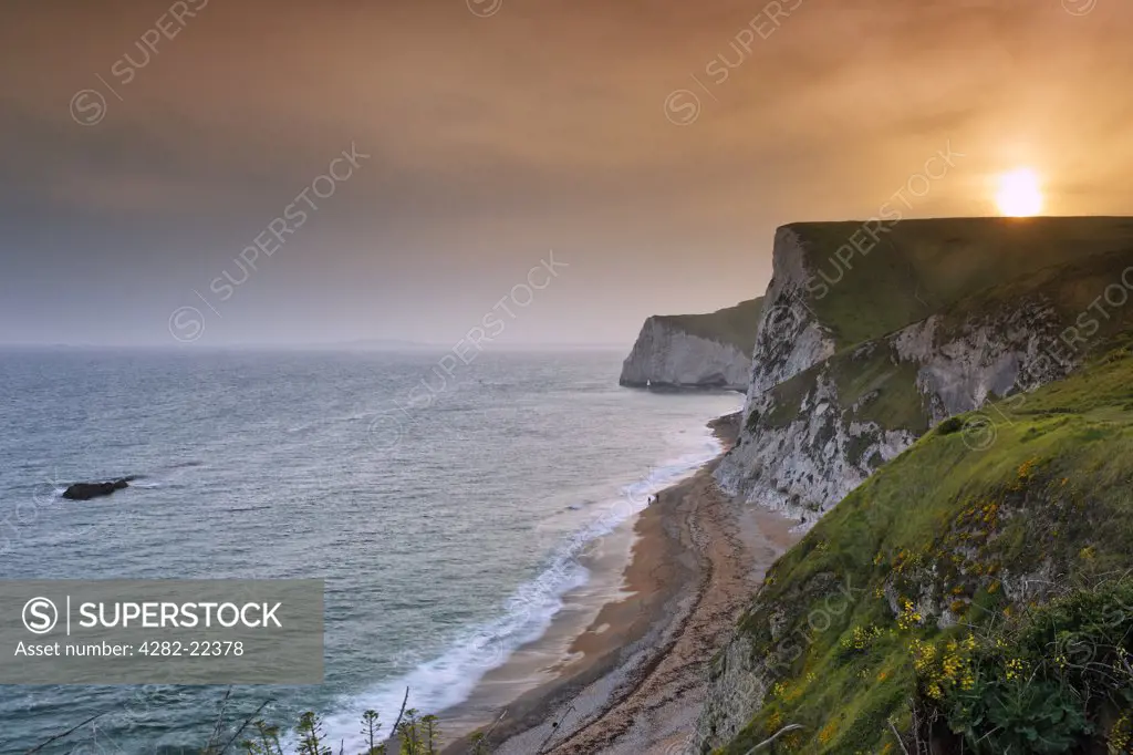 England, Dorset, near Chaldon Herring. Sunset from above Durdle Door looking towards Bat's Hole along the Jurassic coast with the Bull rock on left.