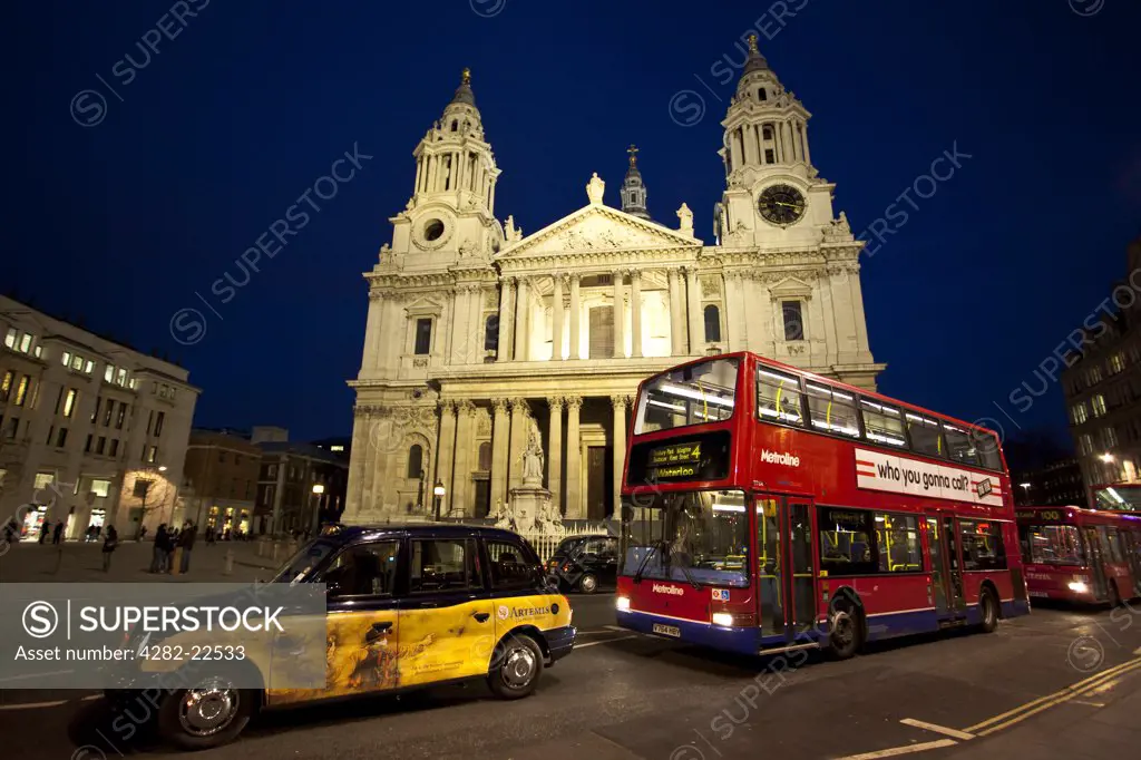 England, London, St Paul's. St Paul's Cathedral lit up at night with a red London bus and taxi in the foreground.