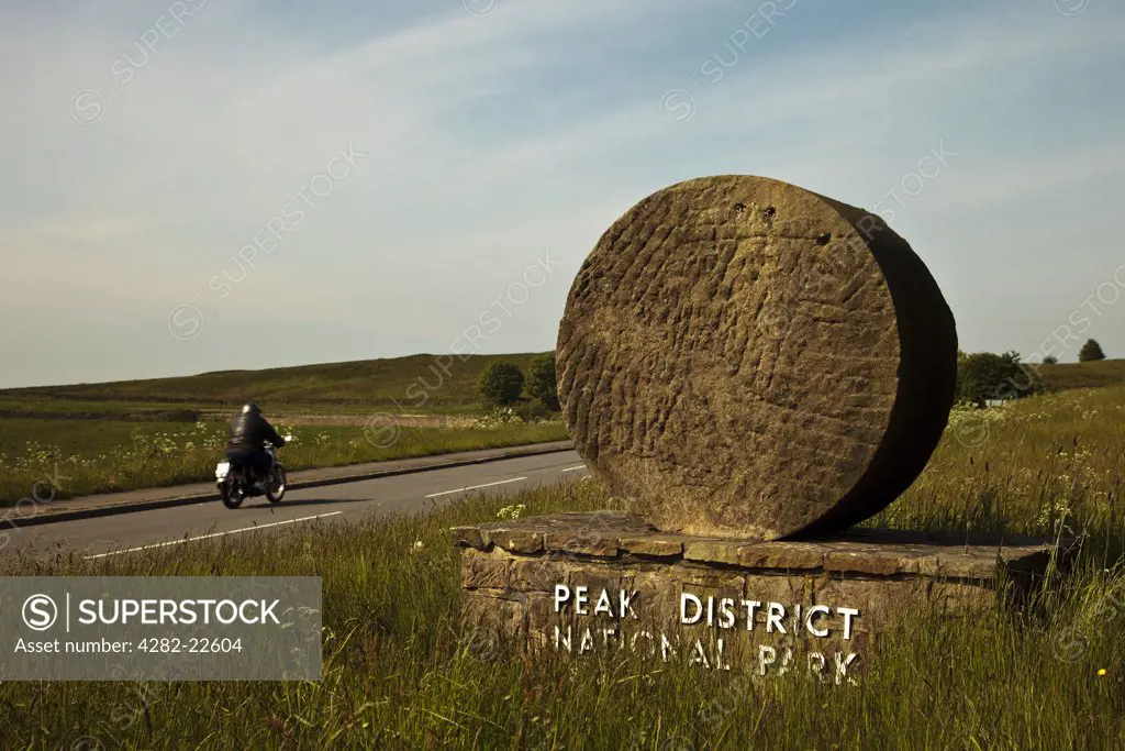 England, Derbyshire, Curbar. A lone motorcyclist rides into the Peak District National Park past one of the stone signs that marks Britain's first national park, established in 1951.