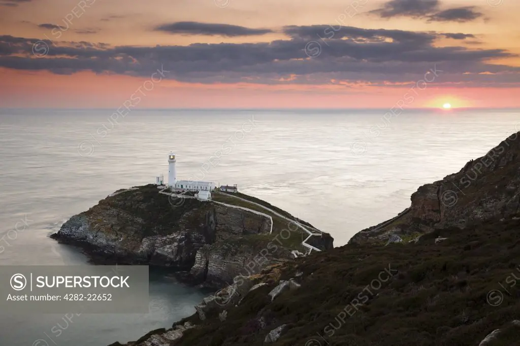 Wales, Anglesey, South Stack. The sun setting on the horizon behind South Stack Lighthouse, a spectacular lighthouse just off Holy Island on the north west coast of Anglesey.