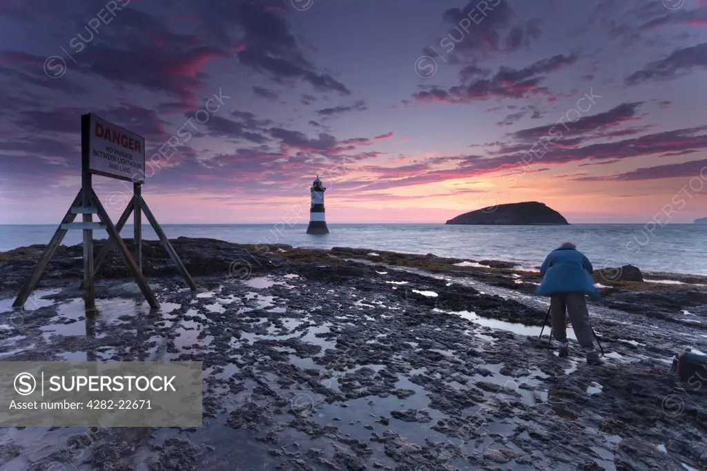 Wales, Anglesey, Penmon. A photographer photographing Penmon Lighthouse and Puffin Island at sunrise.