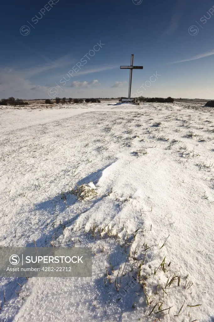England, Norfolk, near Horning. Snow surrounding the massive oak cross standing over the site of the medieval high altar at St Benets Abbey.