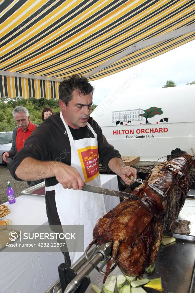 Republic of Ireland, County Monaghan, Scotshouse. Film director Kevin Allen carving a Hilton Orchard Pig Roast. Allen runs Flatlake, a literary/ music festival at Hilton Park, an Irish stately home owned by his in-laws. He has built an eco home in the orchard and keeps a herd of rare-breed pigs.