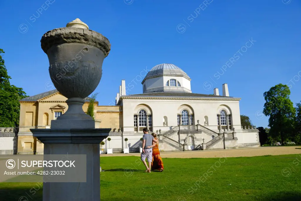 England, London, Chiswick. A couple walking across a lawn at Chiswick House, a neo-Palladian villa built by the third Earl of Burlington in 1729 to showcase his art collection and to enthral his guests.