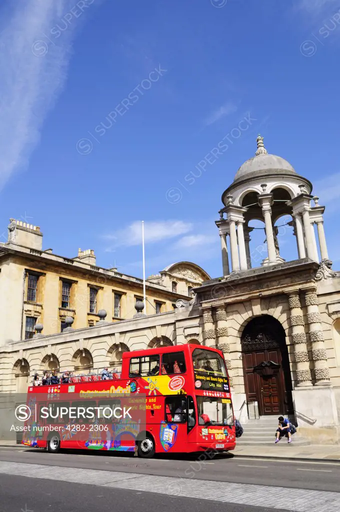 England, Oxfordshire, Oxford. Tourists aboard an open-topped, double decker city sightseeing bus outside The Queen's College, Oxford.