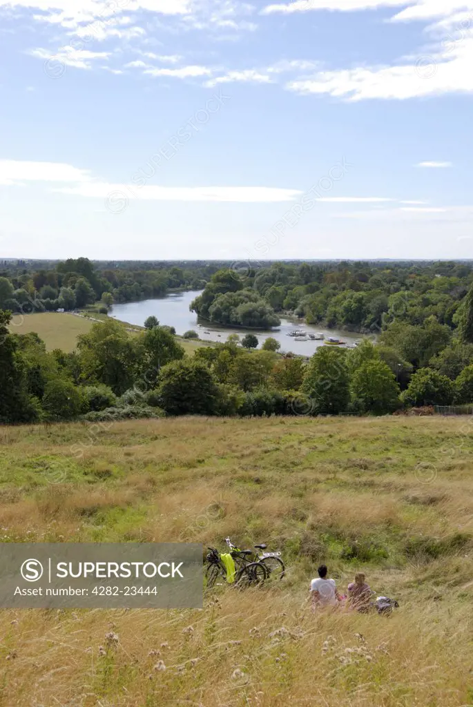 England, London, Richmond-upon-Thames. A couple taking a break from their cycle ride enjoying the view of the River Thames from Richmond Hill.