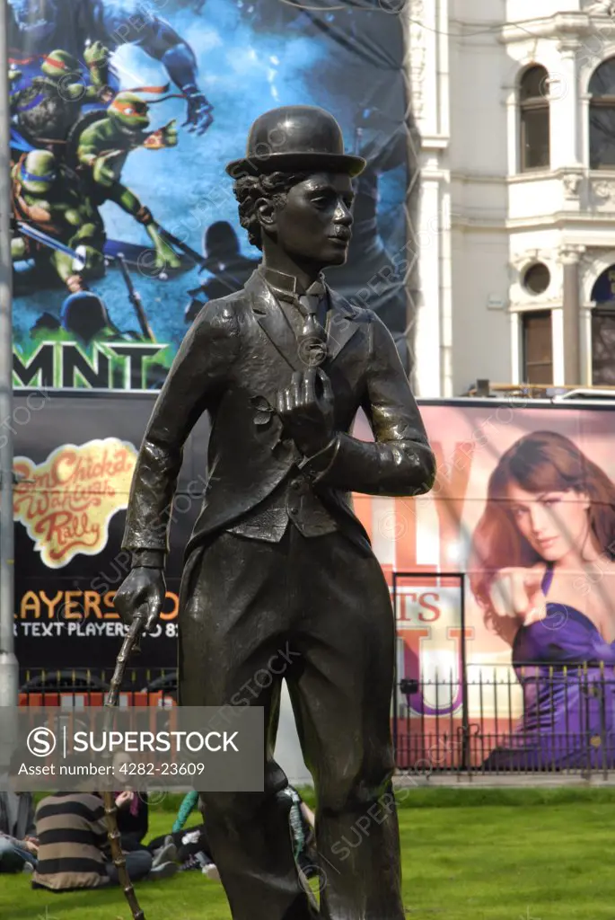 England, London, Leicester Square. Statue of Charlie Chaplin against background of colourful cinema posters in Leicester Square.