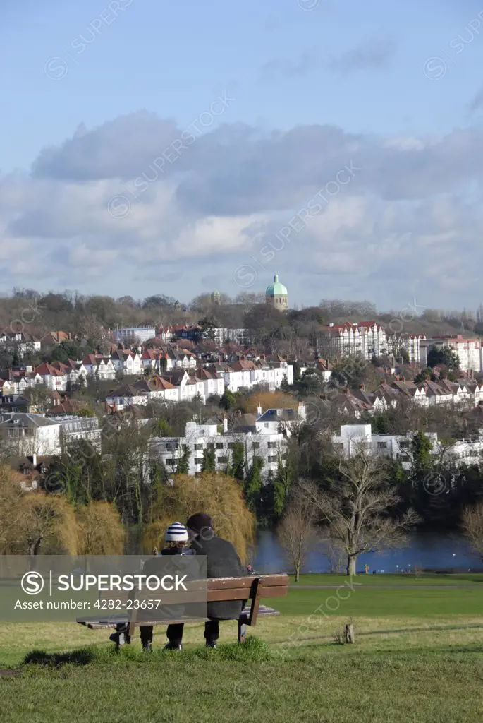 England, London, Hampstead. A couple sitting on a bench admiring the view towards Highgate from Hampstead Heath.