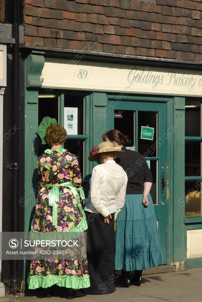 England, Kent, Rochester. Three woman in Dickensian costume looking into a bakery on Rochester High Street during Dickens Festival.
