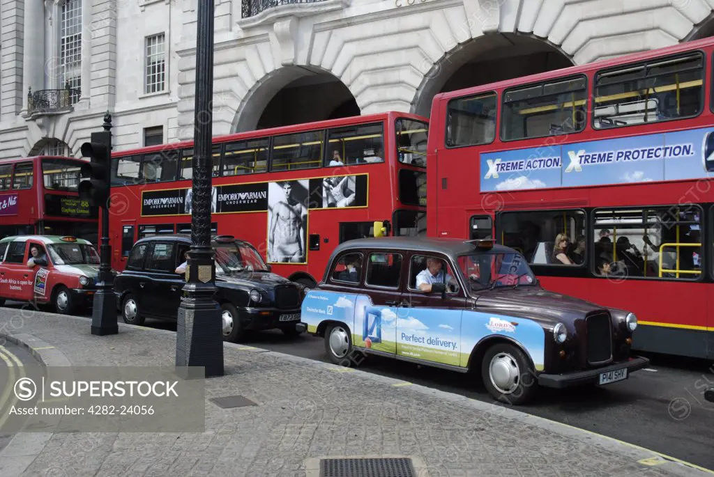 England, London, Piccadilly Circus. Three traditional London taxi cabs and three red London buses with elegant Victorian buildings in the background.