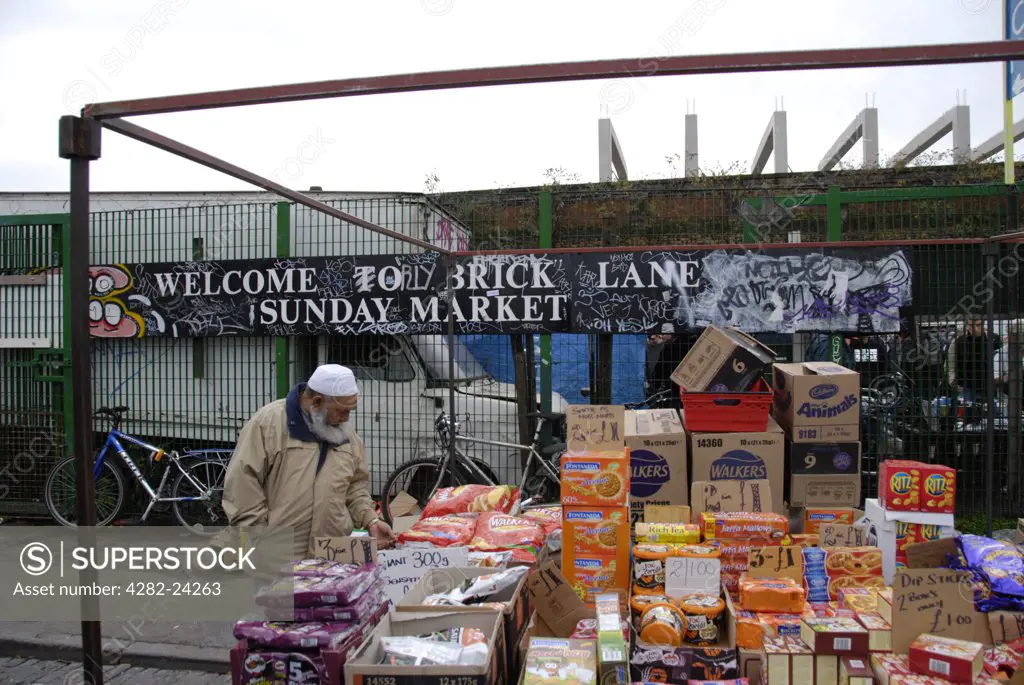 England, London, Brick Lane. An Asian Muslim man inspecting food on Brick Lane Market stall.