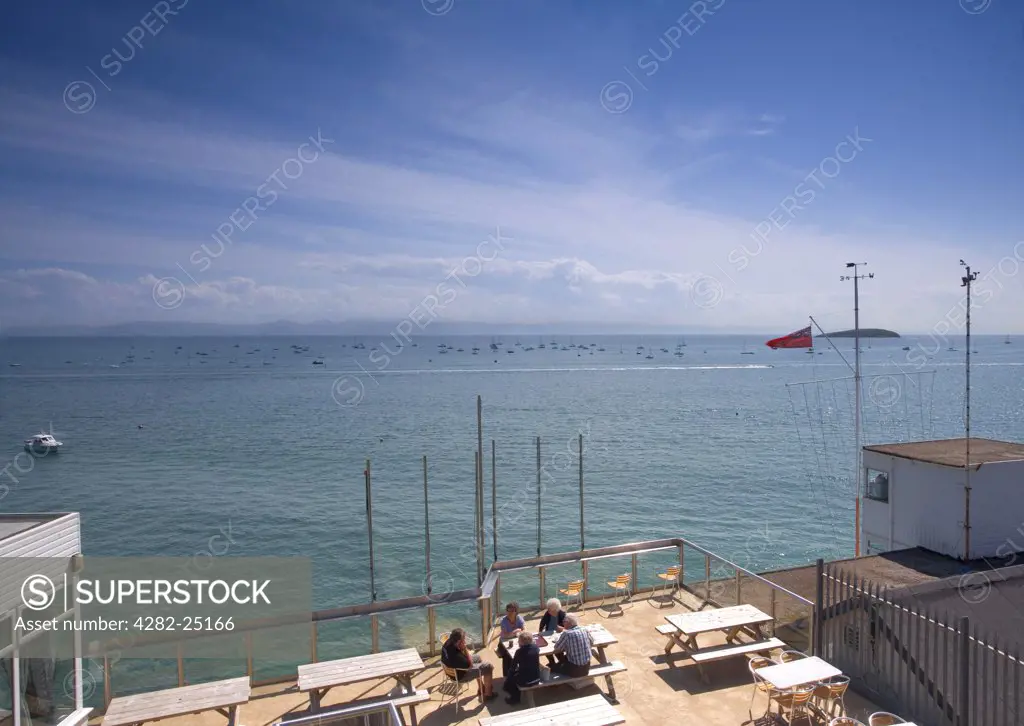 Wales, Gwynedd, Abersoch. A group of people sitting at a table outside a cafe enjoying the view out to sea at Abersoch.