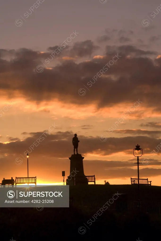 England, North Yorkshire, Whitby. Sunset over a monument to Captain James Cook overlooking Whitby Harbour.