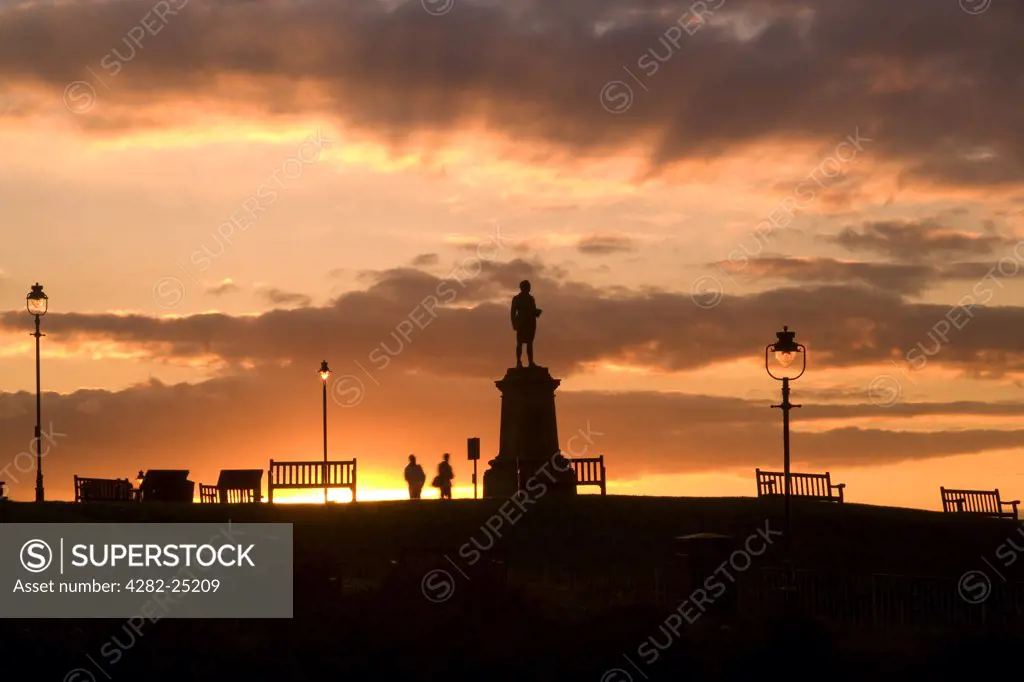 England, North Yorkshire, Whitby. Sunset over a monument to Captain James Cook overlooking Whitby Harbour.