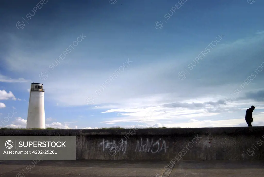 England, Merseyside, Wallassey. Silhouette of a boy standing on a wall.