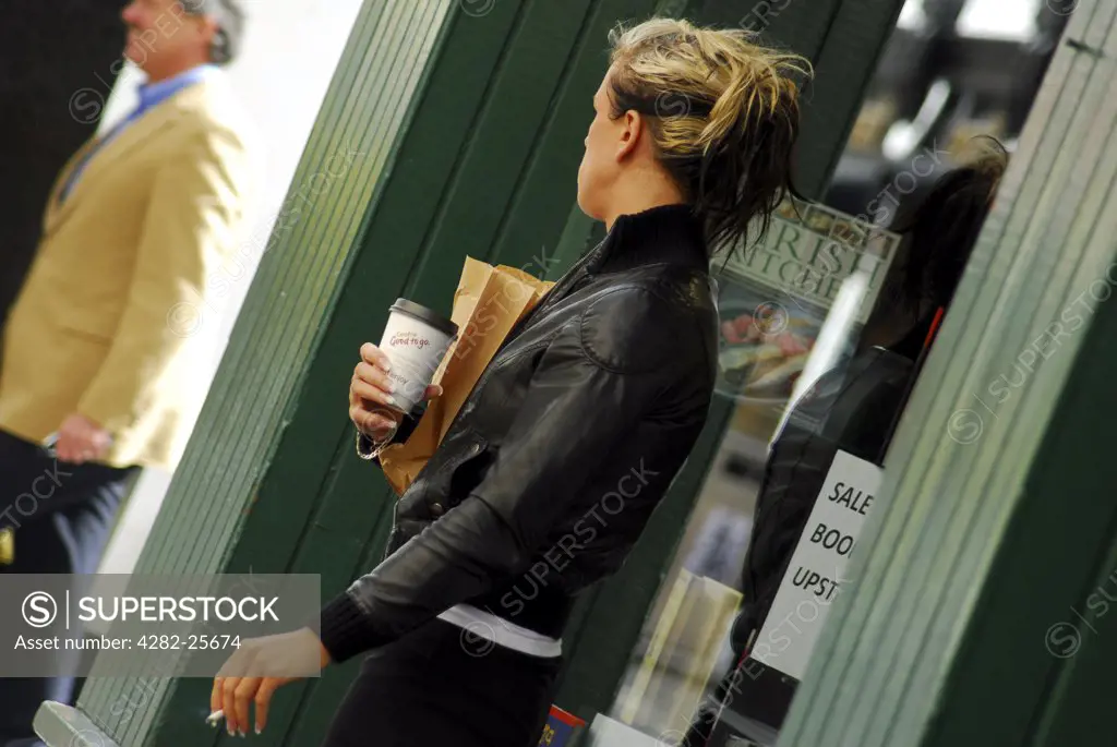 Republic of Ireland, County Cork, Central Cork. A woman with a cigarette and coffee  outside a shop in central Cork.