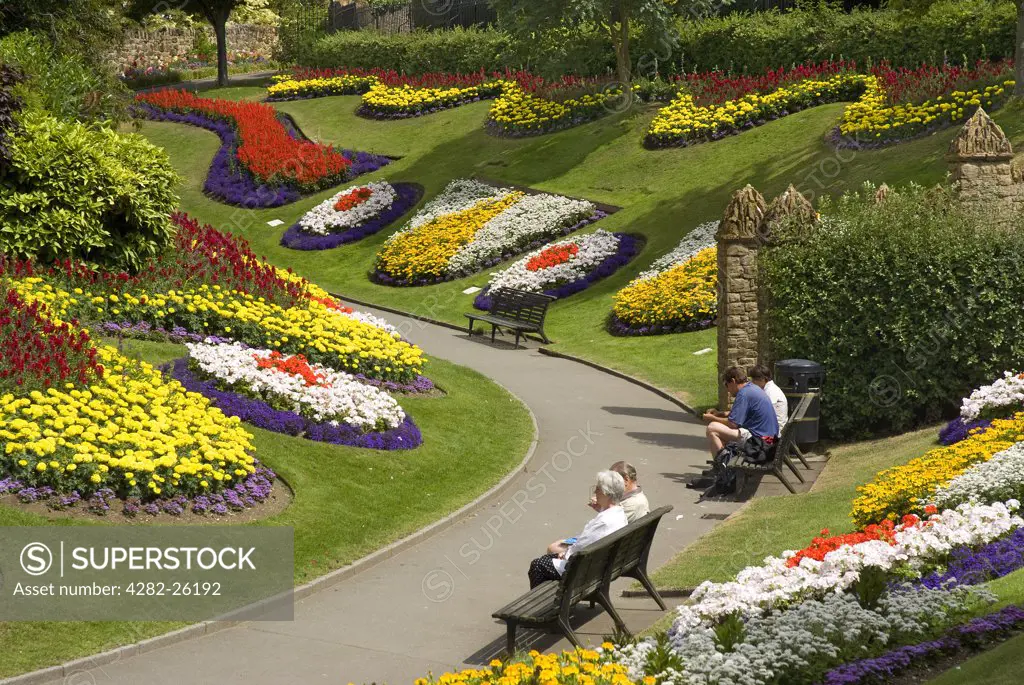 England, Surrey, Guildford. People sitting on benches amongst a stunning floral display in the grounds of Guildford Castle.