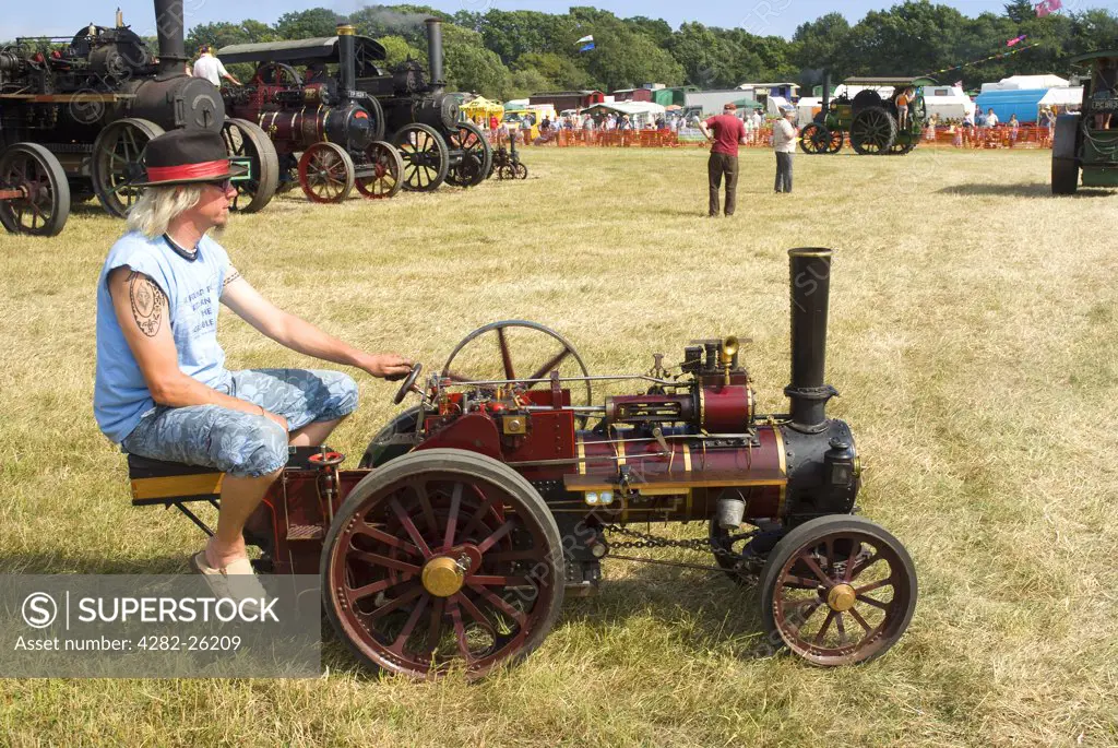 England, East Sussex, Ringmer. A man sitting on a miniature steam traction engine at the Ringmer Steam & Country Show.