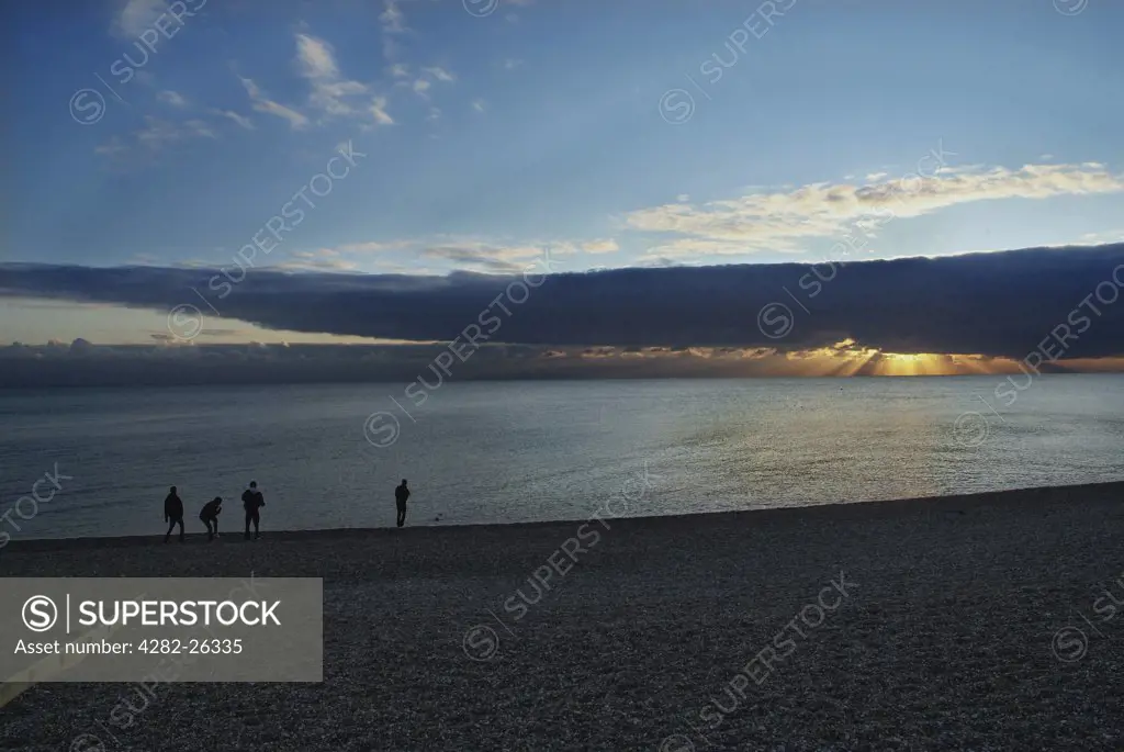 England, City of Brighton and Hove, Hove. Young men skimming stones into the sea on Hove beach at sunset.