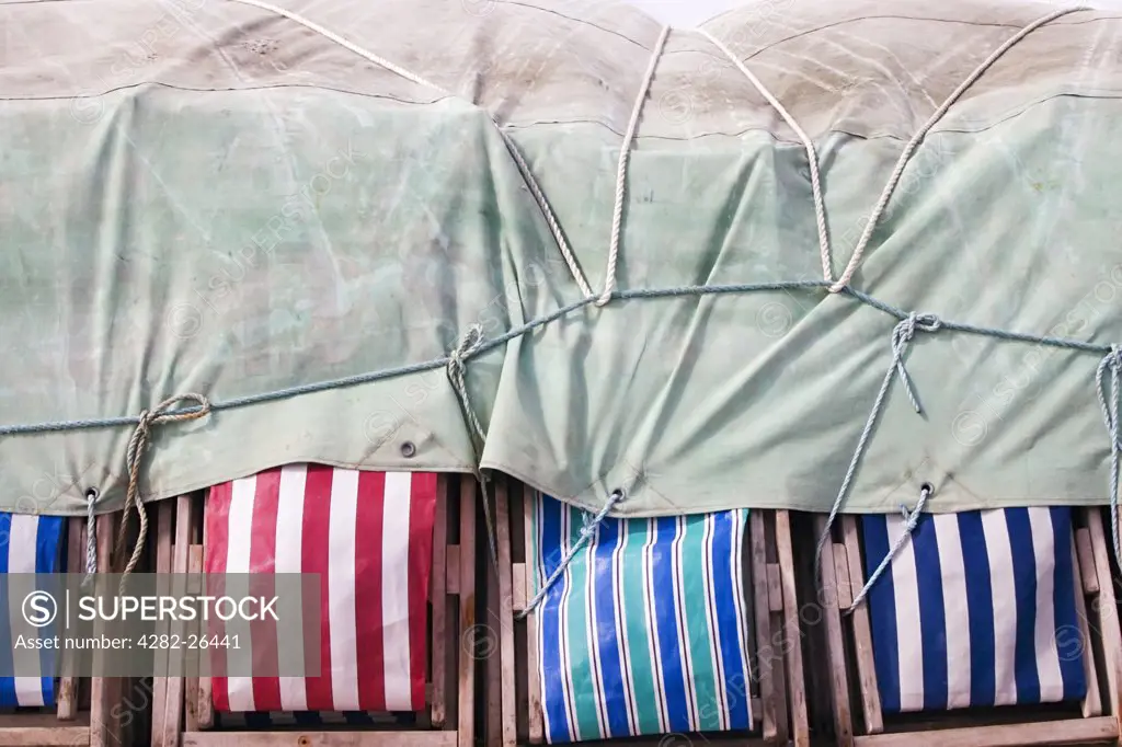 England, Lancashire, Blackpool. Striped deckchairs stacked and tied under a cover in Blackpool.