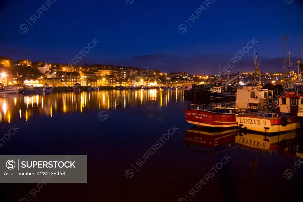 England, North Yorkshire, Whitby. Boats and lights reflected on the water in Whitby harbour.