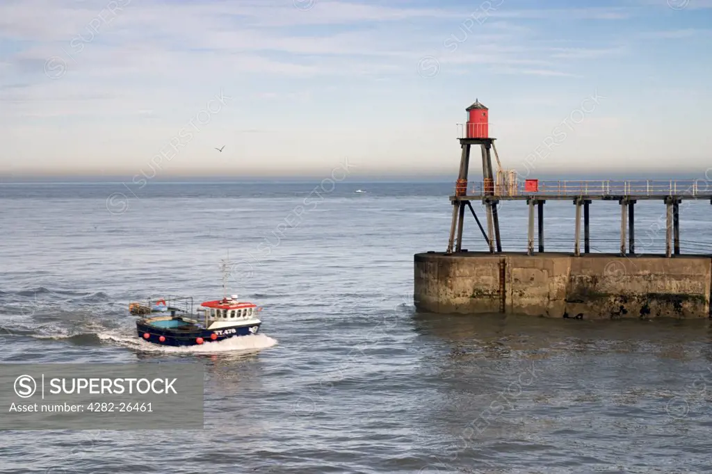 England, North Yorkshire, Whitby. Fishing boat sails past the pier into Whitby harbour.