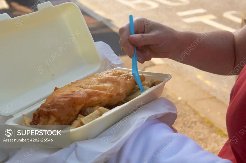 England, Lancashire, Morecambe. A close up of a woman eating fish and chips from a tray on Morecambe sea front.