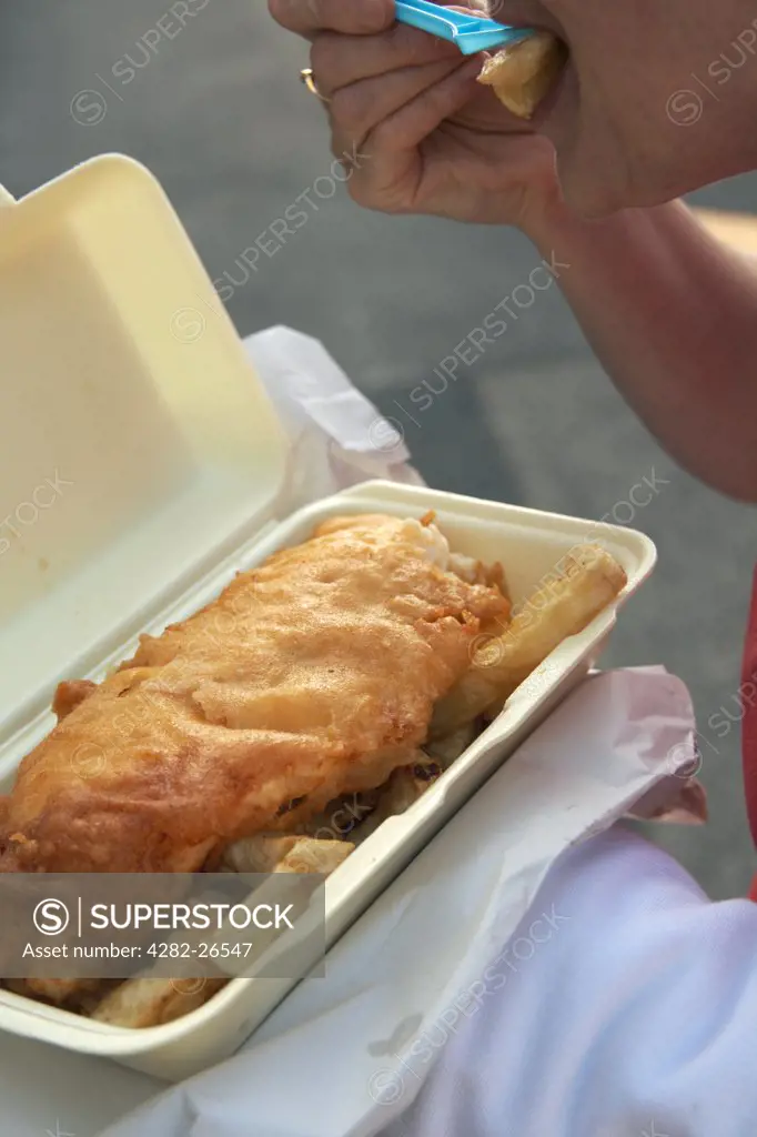 England, Lancashire, Morecambe. A close up of a woman eating fish and chips from a tray on Morecambe sea front.
